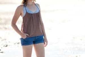 Woman wearing blue lace bralette with brown spaghetti strap tank and denim cuff shorts