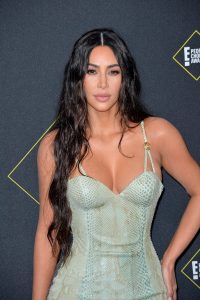 Kim Kardashian with long wavy hair wears a mint-colored snakeskin outfit with a low-cut neckline at an event