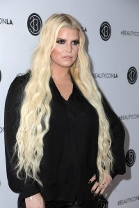 Jessica Simpson with long curly blonde hair wearing black long sleeves and black pants in an event place