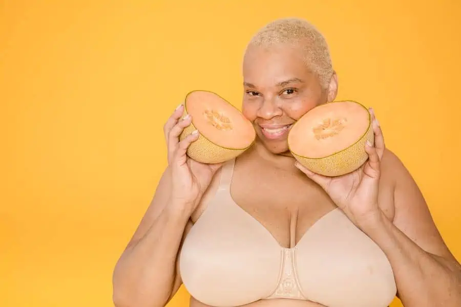 Woman holding melons cut in half while wearing a nude bra