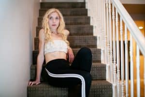 A white bandeau strapless bralette and black jogging pants are worn by a woman seated on the stairs