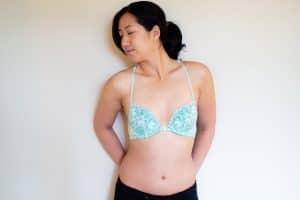 A woman wearing a green lined underwired bra with a floral lace design leaning on a white wall