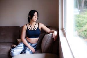 A woman wearing a blue high-neck bralette and colorful leggings is seated on a brown couch