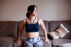A dark blue racerback sports bra and leggings are worn by a woman seated on a brown couch