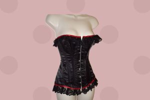 A black corset with a red lining and ruffles placed on a white mannequin