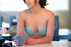 A green racerback underwire bra with a front clasp and adjustable straps worn by a woman holding a blue mug