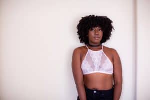 A woman wearing a white high-neck bralette and black jeans standing near a white wall