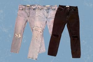 Three different colors of tattered denim jeans are placed on a blue background