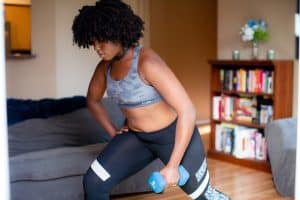 A woman in a sports bra with a camouflage design wearing black leggings using a blue dumbbell to exercise inside a room