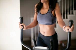 A gray sports bra and black leggings worn by a woman exercising using an elliptical machine