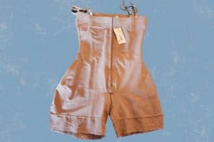 A back view of cream full-body shapewear with snaps and adjustable straps placed on blue background