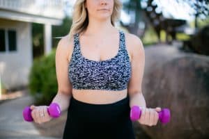 A black and white sports bra and black leggings are worn by a woman using a purple dumbbell