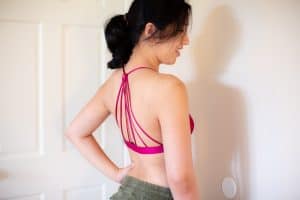 A woman wearing a pink racerback bra and green shorts is standing facing the wall