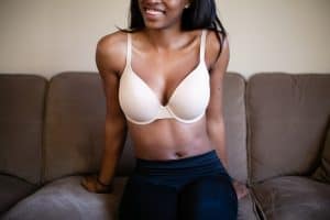 Woman in a white push-up bra with underwire and adjustable straps wearing black leggings seated on a brown couch