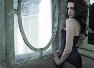 Anne Hathaway wearing a black corset and black lace underwear standing near a window