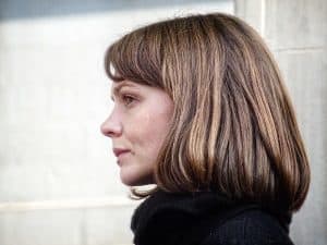 A side view of Carey Mulligan wearing a black scarf and black long sleeves