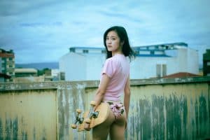 A woman on a rooftop wearing a pink shirt and panty while holding a skateboard