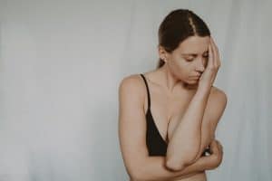 A woman wearing a bra slouching a little bit while her hands touching her face