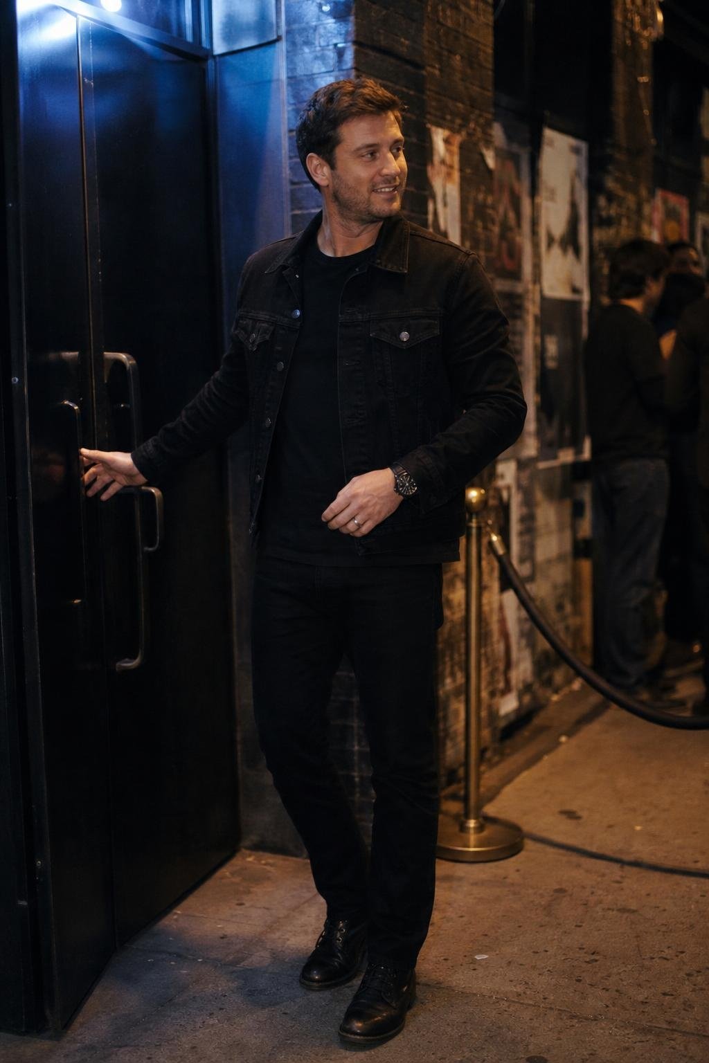 Black denim jacket, black tee, black straight jeans, black leather boots, late-night concert venue entrance (option 2)