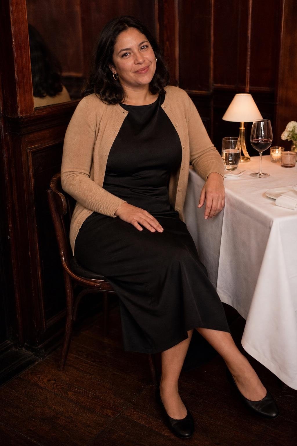 Black sleeveless midi dress, camel cardigan, black flats, gold hoops, intimate restaurant corner table (option 2)