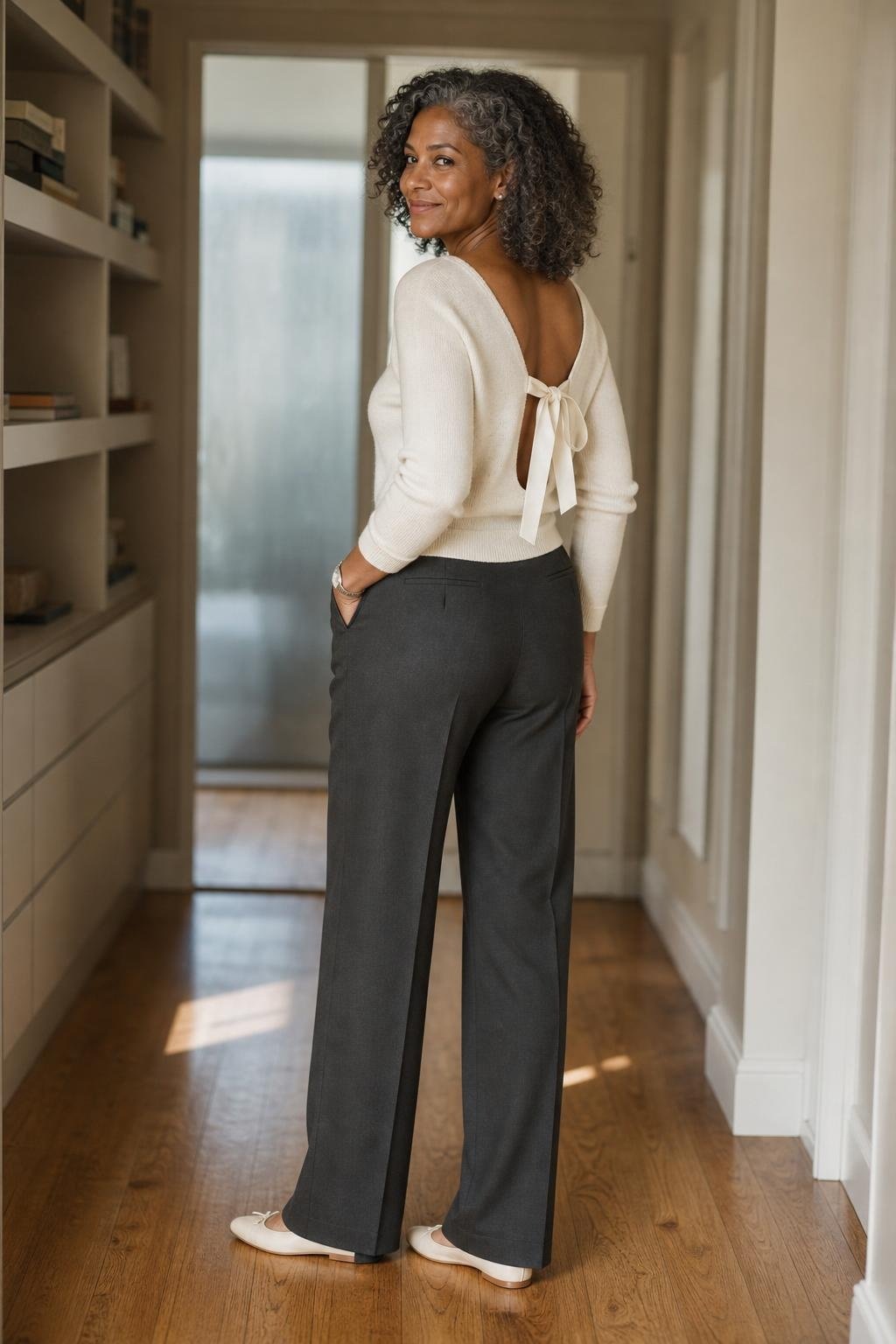 cream bow-back sweater, charcoal tailored trousers, satin flats, softly lit office hallway (option 2)