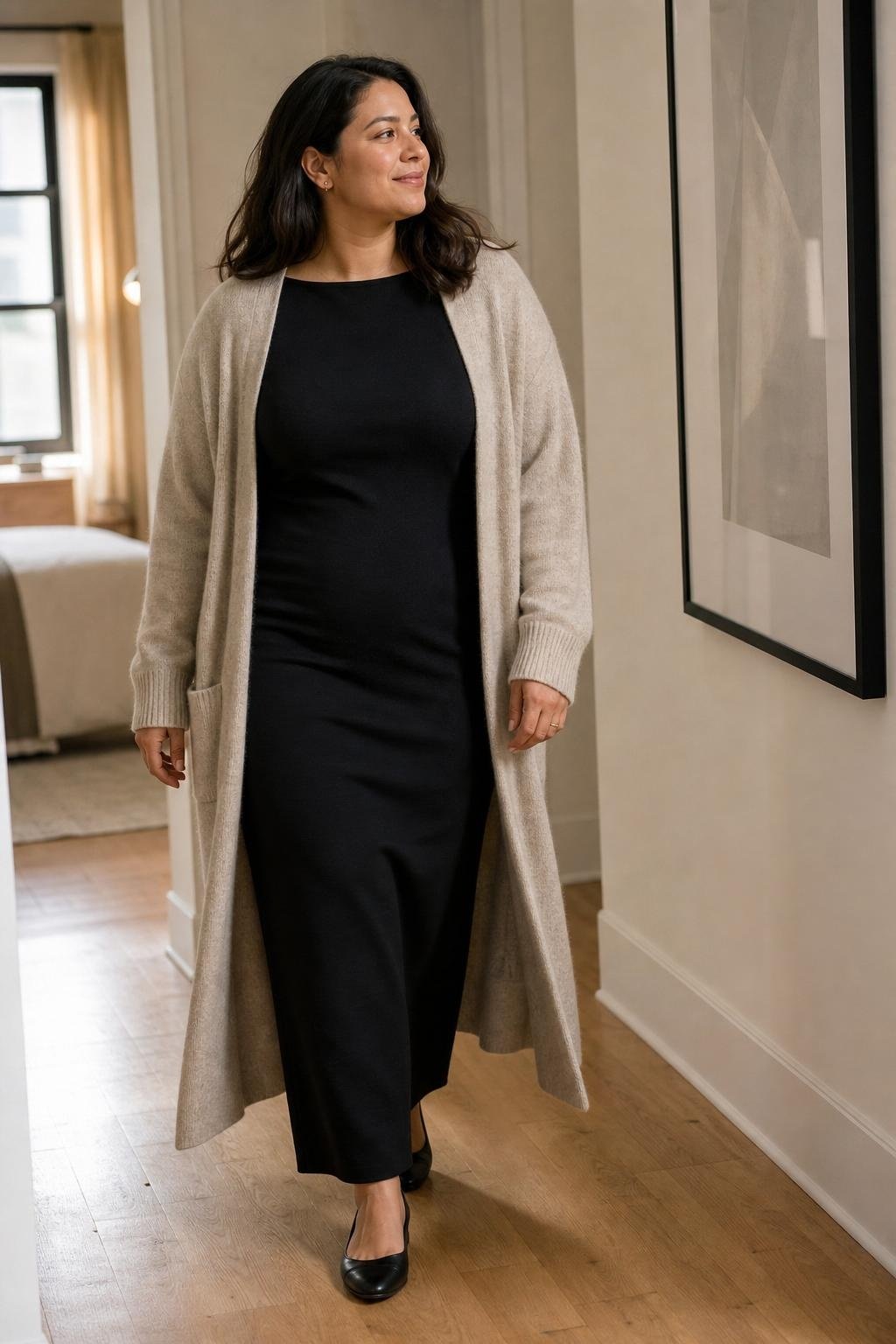 Simple black column dress, long oatmeal cardigan, black flats, minimal gallery hallway (option 1)