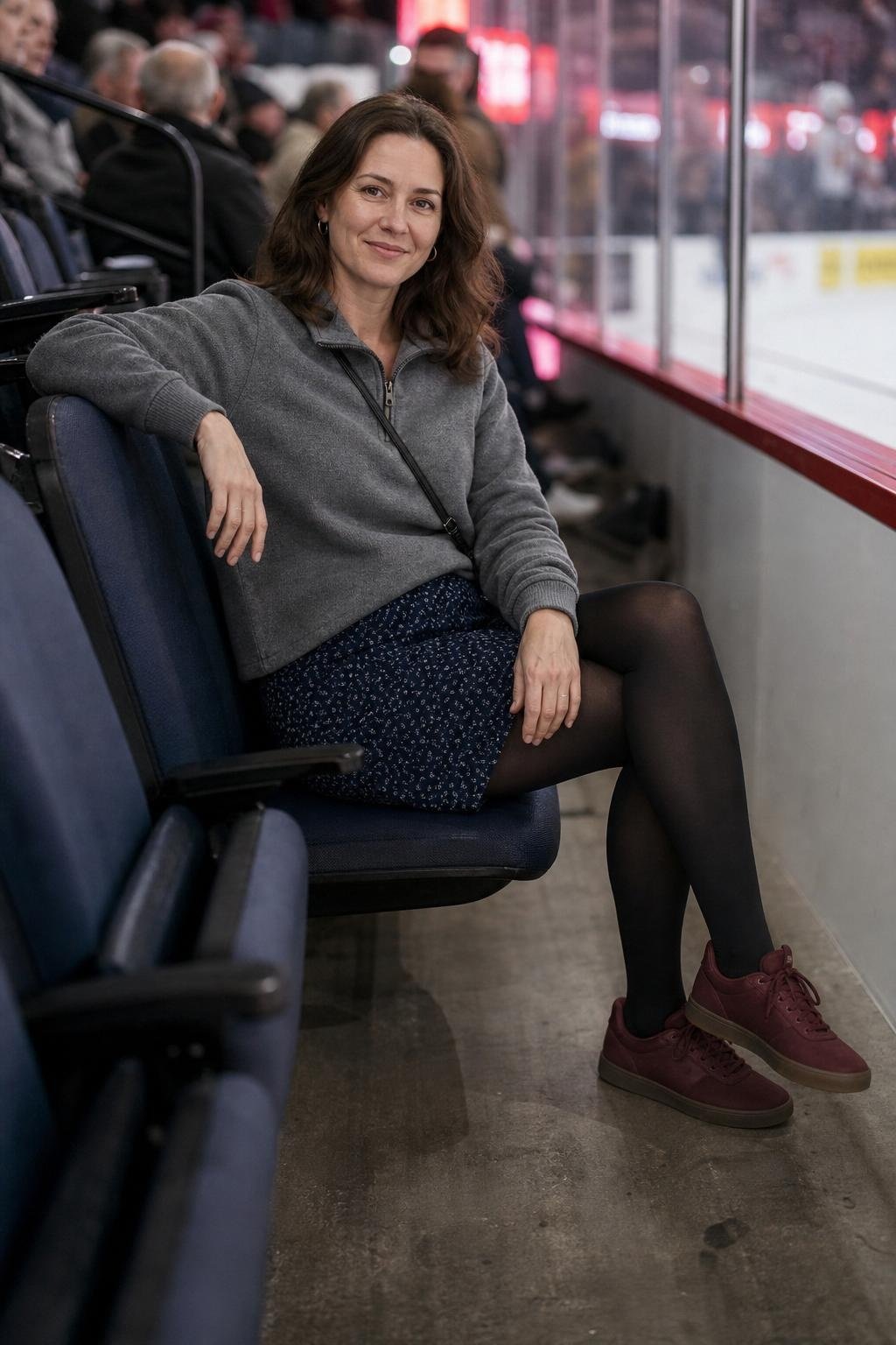 Slate gray fleece pullover, navy printed skirt, black tights, dark red sneakers, cozy indoor arena seating (option 2)