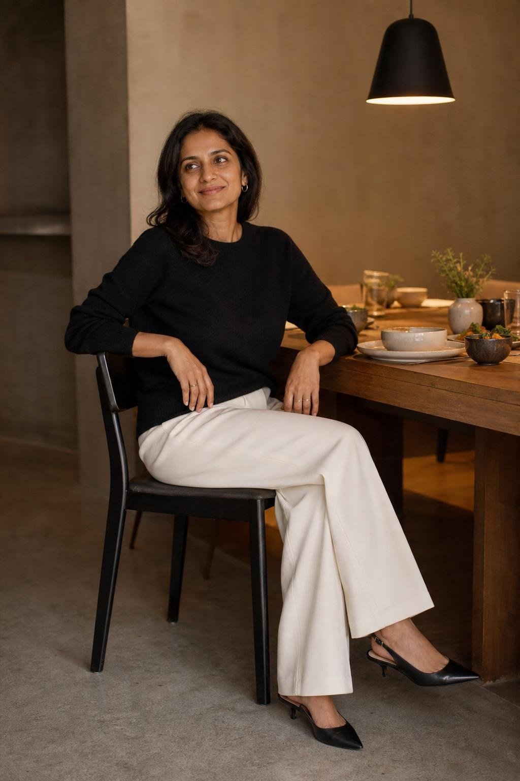 Soft black cashmere sweater, ivory wide-leg trousers, black slingbacks, calm dinner table setting (option 2)