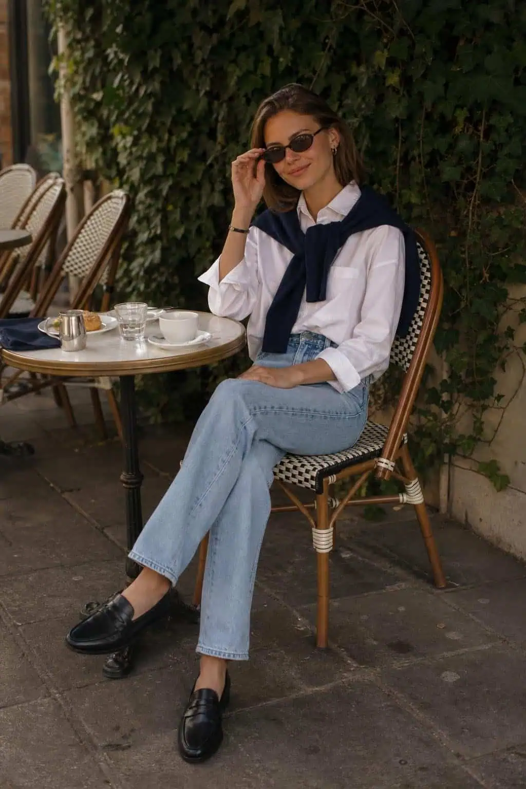 White poplin shirt, navy sweatshirt over shoulders, light straight jeans, loafers at an outdoor café (option 1)