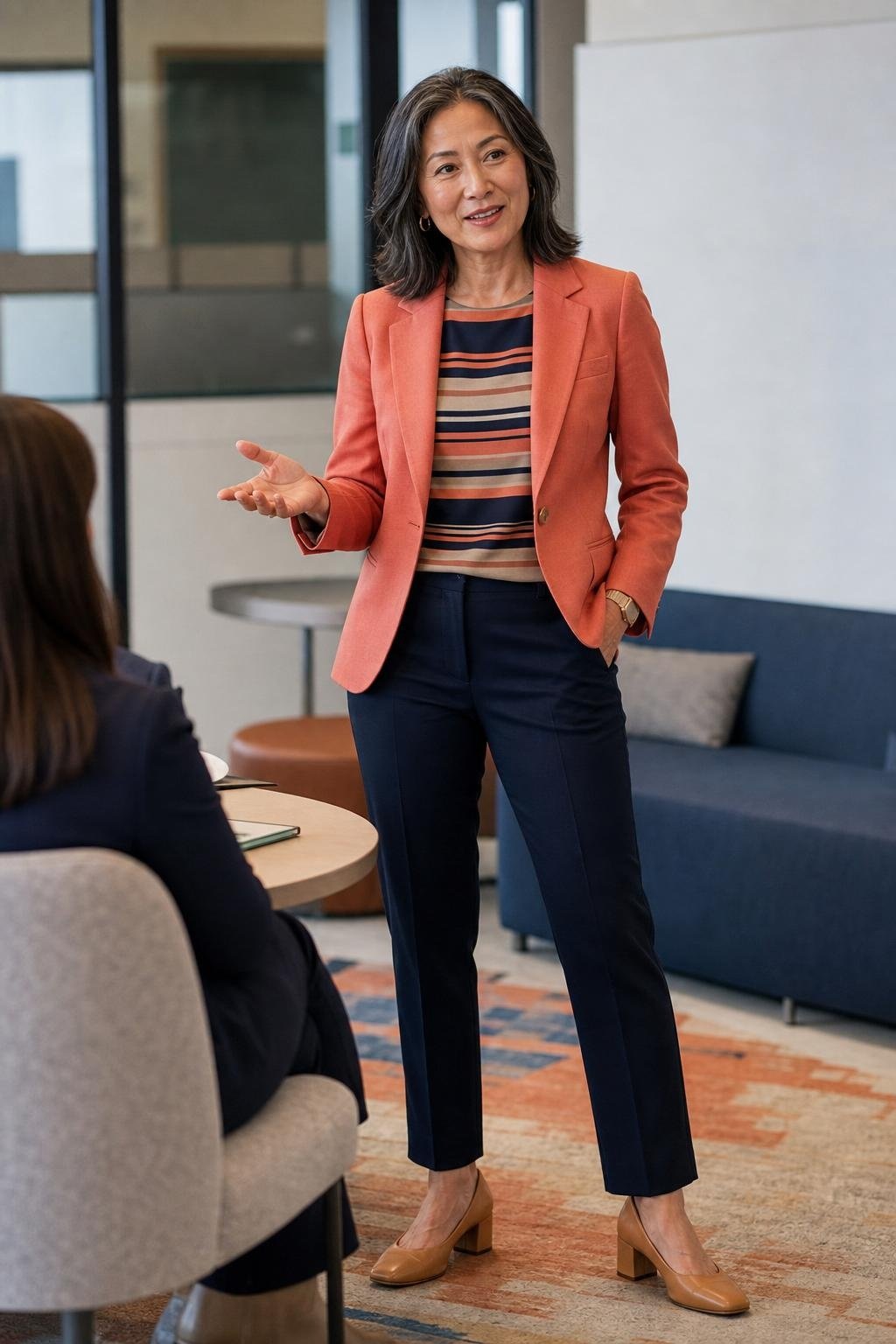 coral blazer, navy ankle pants, striped shell, tan block heels, lively office meeting area with crisp color mood (option 2)